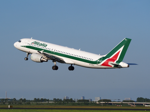 Ein Airbus A320-232 ERJ-EJZ der Alitalia startet vom Frankfurter Flughafen mit grünem Gras, B├Ąumen, Geb├Ąuden und einem klaren blauen Himmel im Hintergrund.