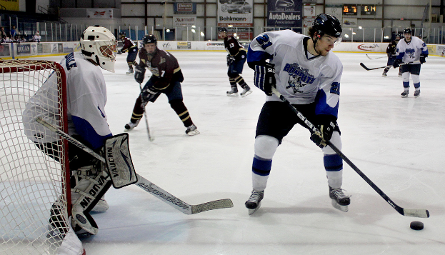 Eine Gruppe junger Männer, die Eishockey auf einem Eisplatz spielen, tragen Helme und halten Hockey-Schläger, mit einem Torpfosten links und Bannern im Hintergrund.