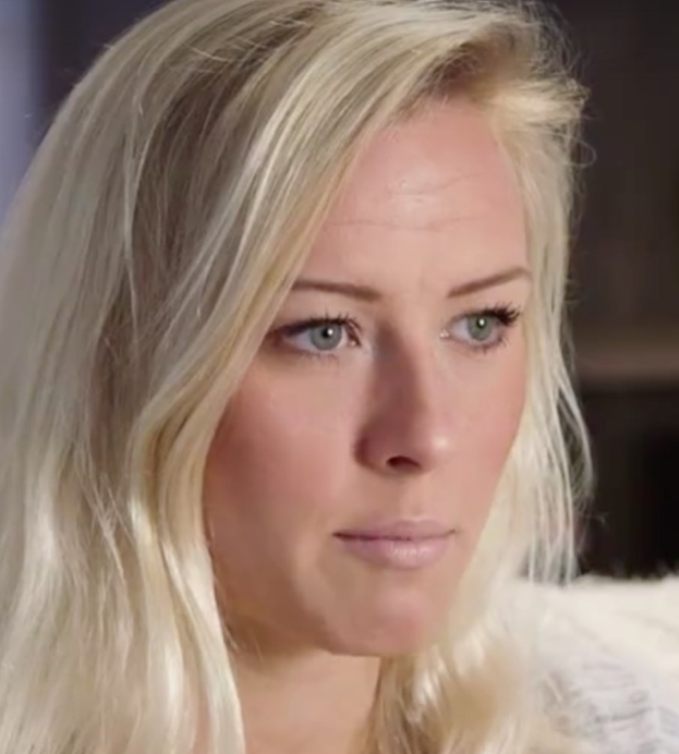 Eine Frau mit langen blonden Haaren und blauen Augen im Vordergrund, die besorgt wirkt mit einem unscharfen Hintergrund.