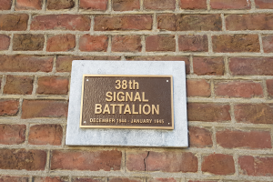 Eine Ziegelwand mit einer rechteckigen Plakette, auf der in fetter, weißer, zentrierter Schrift "38. Signal Battalion" steht.