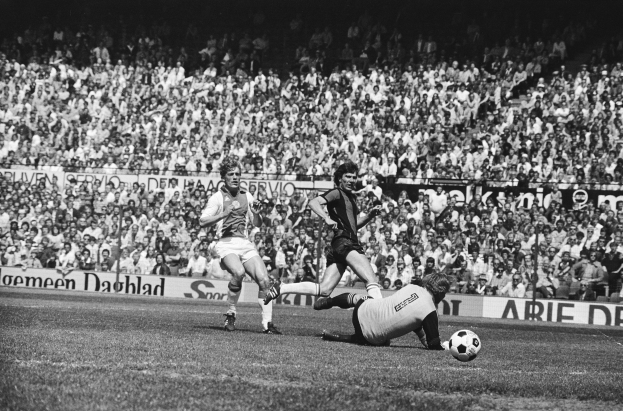 Schwarz-weißes Foto von Männern, die auf einem Feld Füßball spielen, mit Zuschauern im Hintergrund und einem Banner mit der Aufschrift "Bundesliga 1978-79 Ajax 1-1 Hannover 96".