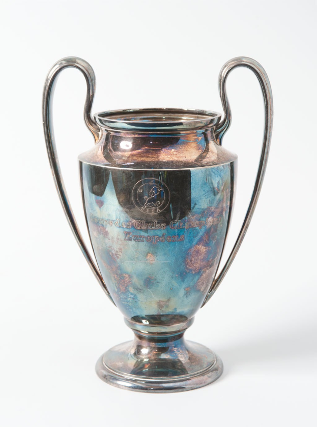 Ein glänzender UEFA Champions League Pokal in Silber und Blau mit zwei Griffen, darauf eingraviert 'UEFA Champions League', vor einem weißen Hintergrund.
