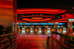 Ein Casino-Innere mit einem Weihnachtsbaum in der Mitte, gefliesten Böden, Geländern auf beiden Seiten, geschmückten Säulen und Deckenlampen, mit Menschen im Hintergrund, die eine festliche Atmosphäre schaffen.