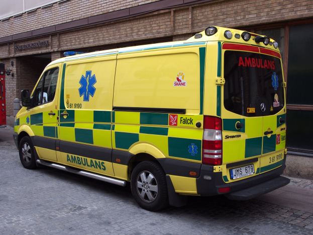 Ein Rettungswagen steht auf der Straße vor einem Backsteingebäude mit Text darauf, und ein Feuerlöscher befindet sich auf der linken Seite des Bildes.