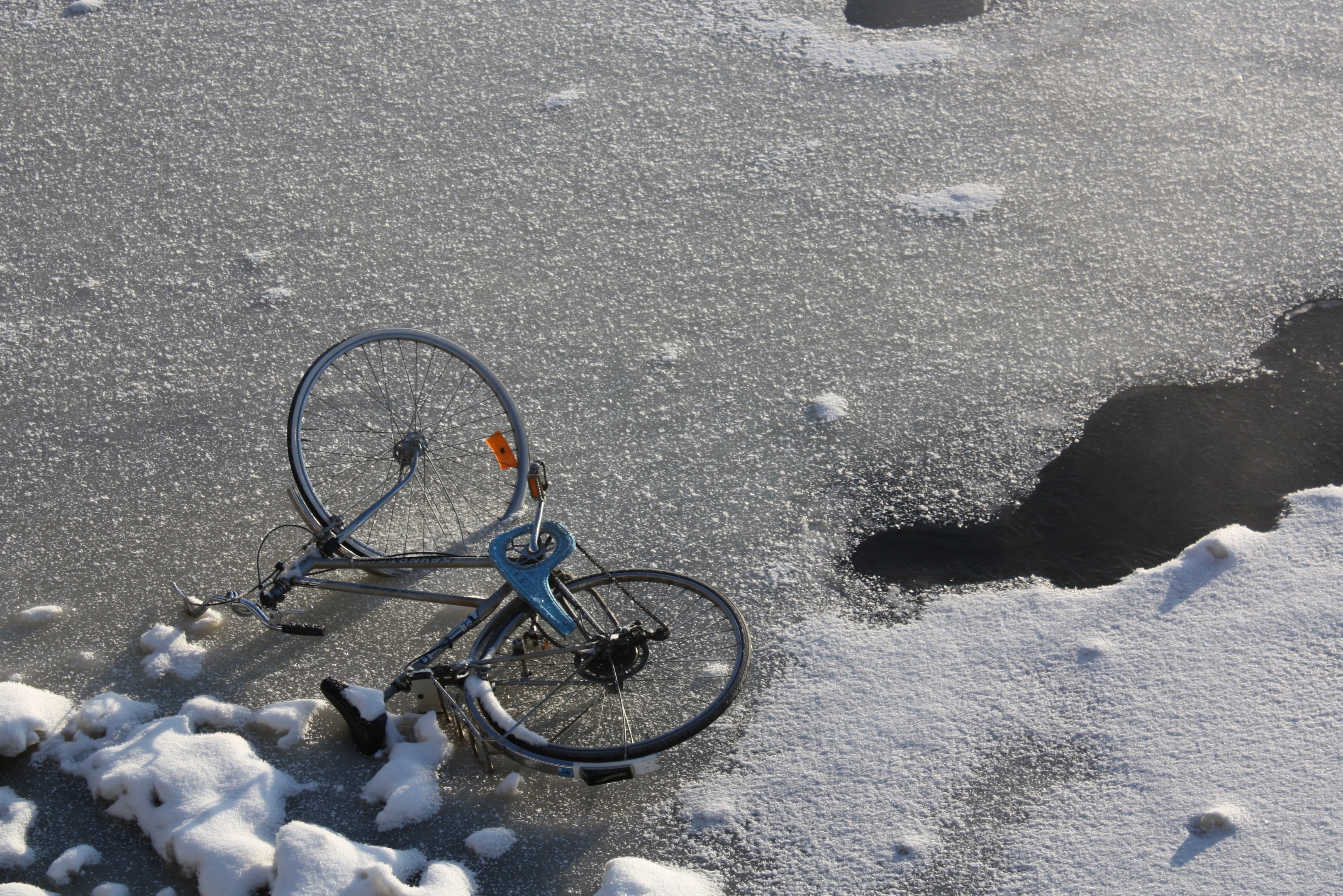 Ein Fahrrad liegt im Schnee neben einer Pfütze Wasser, mit einer Schneedecke drumherum.