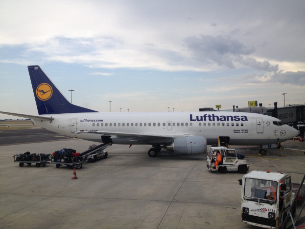 Lufthansa Airbus A320-200 am Frankfurter Flughafen mit Bodenfahrzeugen, Verkehrskegeln und Informationsschildern unter einem bewölkten Himmel.