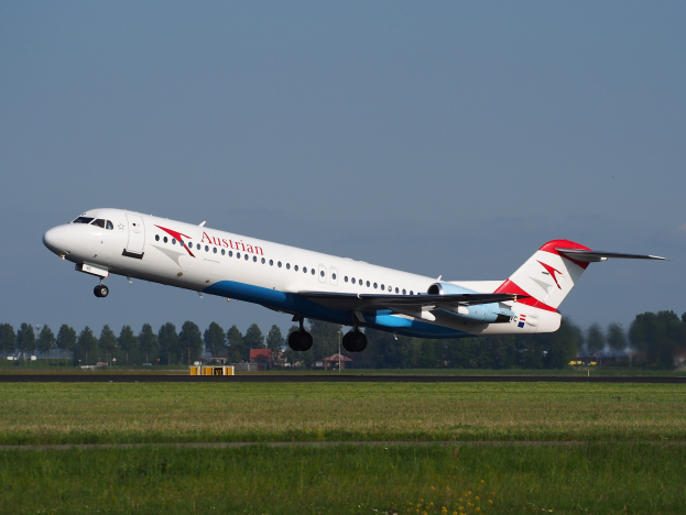 Ein Embraer ERJ-190 der Austrian Airlines beim Start vom Frankfurter Flughafen, mit grünem Gras, Bäumen, Gebäuden und Himmel im Hintergrund.