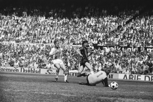 Schwarzes und weißes Foto von Fußballspielern auf einem Feld während eines Bundesligaspiels zwischen Ajax und Hannover 96 in der Saison 1978-79, mit Zuschauern im Hintergrund.