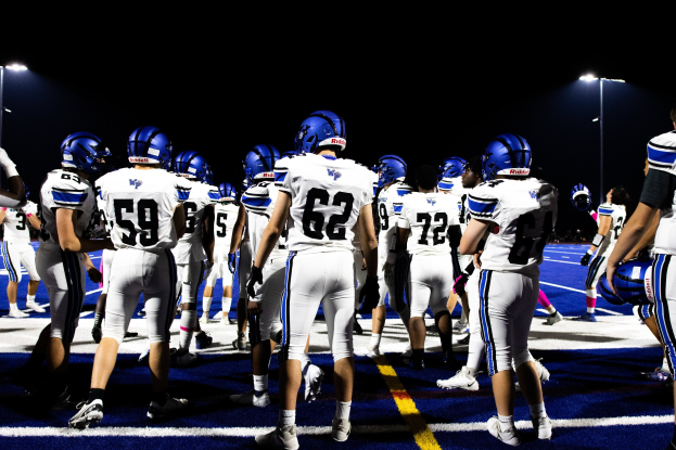 Eine Gruppe von Füßballspielern in Helmen und Stiefeln, die auf einem Feld unter Flutlicht stehen.