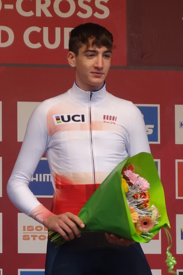 Ein Mann steht triumphierend auf einem Podium, hält einen Blumenstrauß in der Hand und hat eine Tafel im Hintergrund, die Freude und Erfolg ausstrahlt.