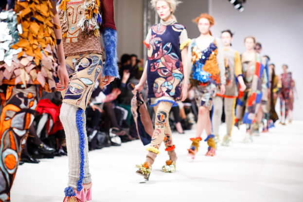 Eine Gruppe Von Frauen, Die Auf Einer Laufsteg In London Fashion Week Gehen, Mit Sitzenden Zuschauern Und Bühnenbeleuchtung Im Hintergrund.