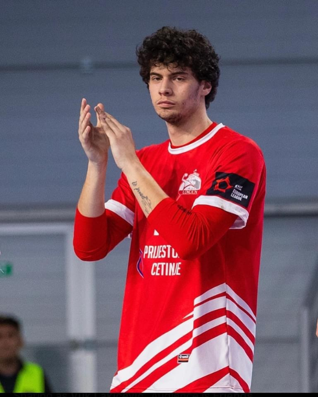 Ein Mann in rot-weißem T-Shirt klatscht in der Vordergrund, während im Hintergrund eine weitere Person und eine Wand zu sehen sind, Text unten lautet "Copenhagen Futsal Club - Foto 1".