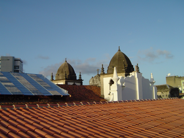 Eine Stadtansicht mit Gebäuden im Vordergrund, Solarpanels auf einem Dach und einem blauen Himmel im Hintergrund.