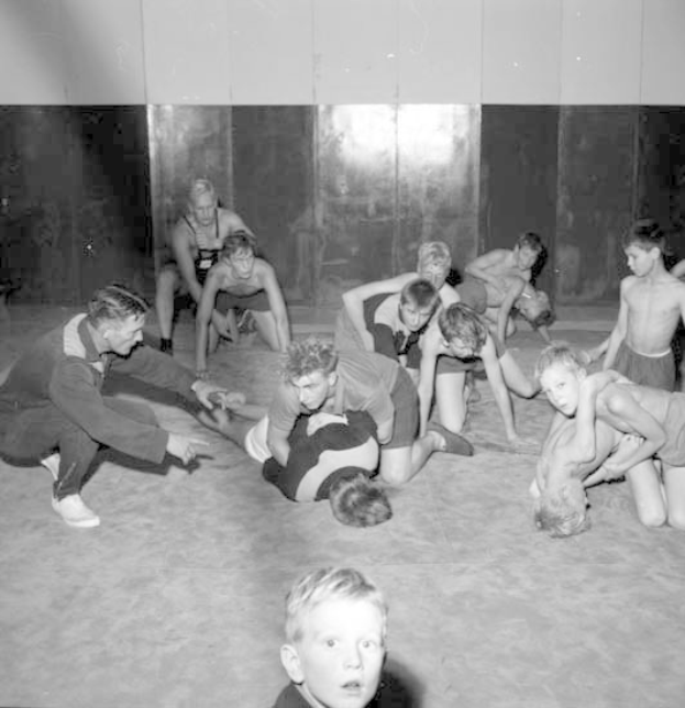 Schwarzes und weißes Bild von jungen Jungs, die in einem Fitnessstudio miteinander ringen, mit einer Wand im Hintergrund.