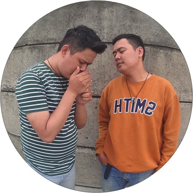 Zwei Männer stehen Seite an Seite, einer in einem orangen T-Shirt und blauen Jeans, der andere in einem grün-weißen gestreiften Hemd, beide wirkend besorgt und in eine heftige Diskussion vertieft.