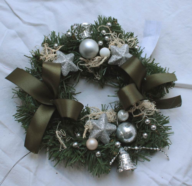 Ein festliches Weihnachtsgesteck mit silbernen Schmuckelementen und Bändern auf einem weißen Tuch, mit bunten Kugeln, Sternen und anderen Dekorationen.