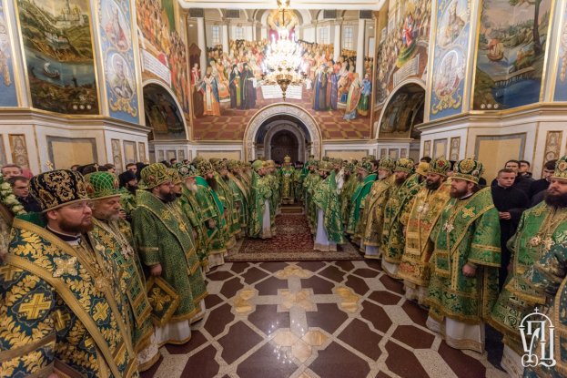 Gruppe von Priestern in grüner und goldener Kleidung, die in einer Kirche mit bemalten Wänden, einem Kronleuchter und einem Bogen in der Hintergrund während einer St. Peters-Feier stehen.