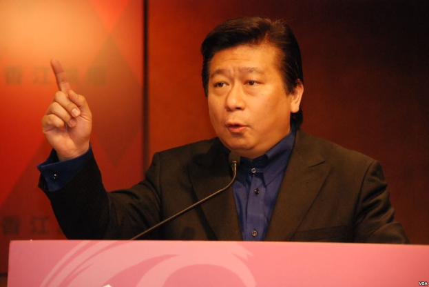 Ein Mann im Anzug und mit Krawatte, der vor einem Rednerpult spricht und ernst dreinschaut.