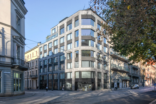 Großes Bürogebäude mit vielen Fenstern, umgeben von Straßeninfrastruktur, Fahrzeugen, Fußgängern, Bäumen und einem bewölkten Himmel, als neuer Firmensitz identifiziert.