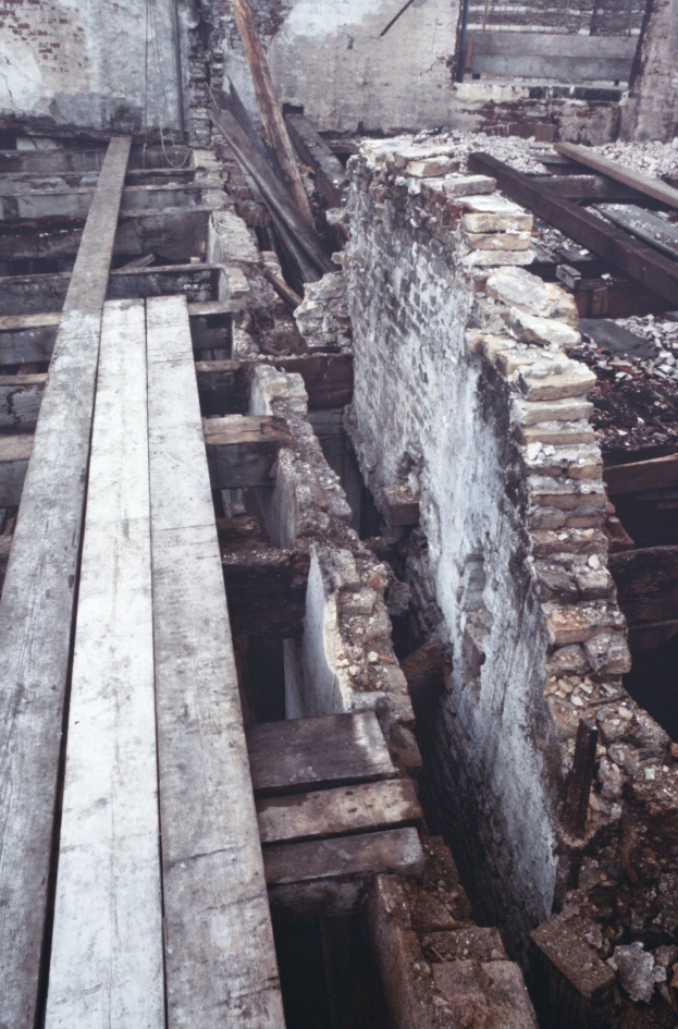 Altbau wird abgerissen mit verstreuten Holzplanken und Steinen im Vordergrund, Backsteinwand im Hintergrund.