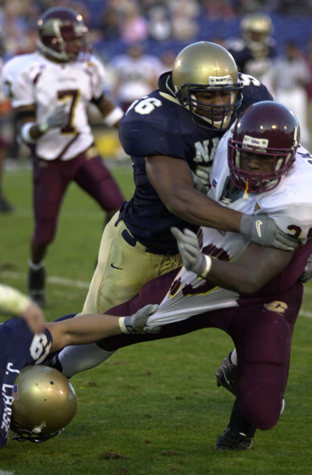 Zwei Fußballspieler in Sportkleidung und Helmen kollidieren auf dem Feld, während andere zusehen.