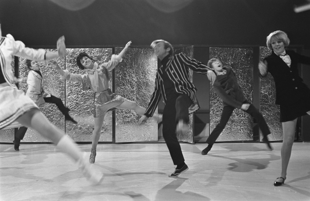 Eine Gruppe von Menschen, die auf einer Bühne tanzen, mit Schuhen, einer Wand im Hintergrund, in Schwarz-Weiß dargestellt.