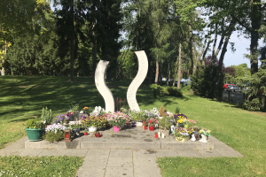 Mahnmal für Opfer des Tschernobyl-Unfalls mit Blumen, Kerzen und umgebender Vegetation in einem Park.