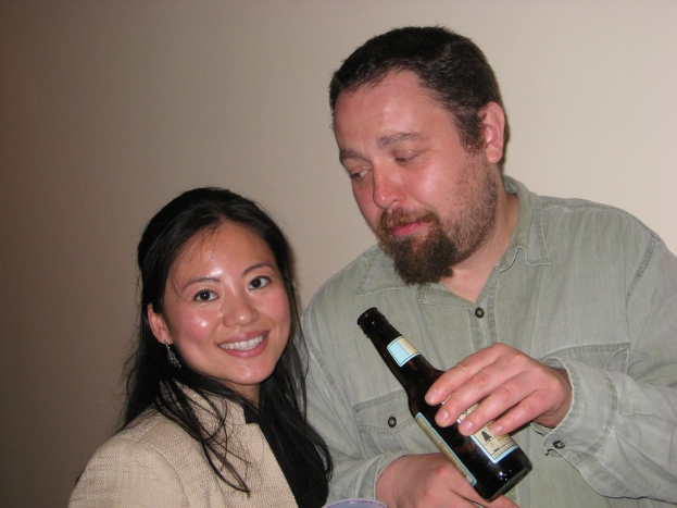 Mann mit Flasche starrt lächelnde Frau vor Wandhintergrund an