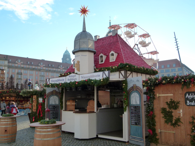 Kleines Gebäude mit rotem Dach und Riesenrad davor, umgeben von Festdekorationen und Menschen bei einem Oktoberfest-Event in München, Deutschland.