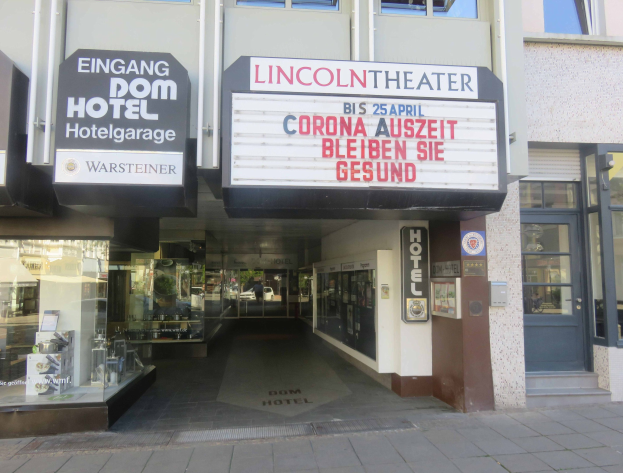Außenansicht des Lincoln Theaters in Berlin, Deutschland, mit Glasfenstern und -türen sowie einer Tafel und einem Inneren, das eine belebte Stadtkulisse vermuten lässt.
