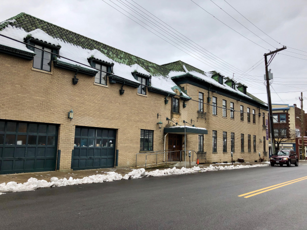Großes Backsteingebäude mit grüner Dachfläche an einer Straßenkreuzung, identifiziert als ehemalige Feuerwache St. Louis, umgeben von Fahrzeugen, Schnee, Strommasten, Bäumen und einem bewölkten Himmel.