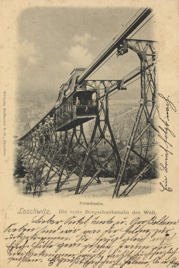 Ein altes Schwarz-Weiß-Foto einer Eisenbahnbrücke mit einem Kran, umgeben von Bäumen und einem bewölkten Himmel, mit Text unten, der besagt: "Bahnstrecka, die erste Eisenbahnbrücke in Deutschland".