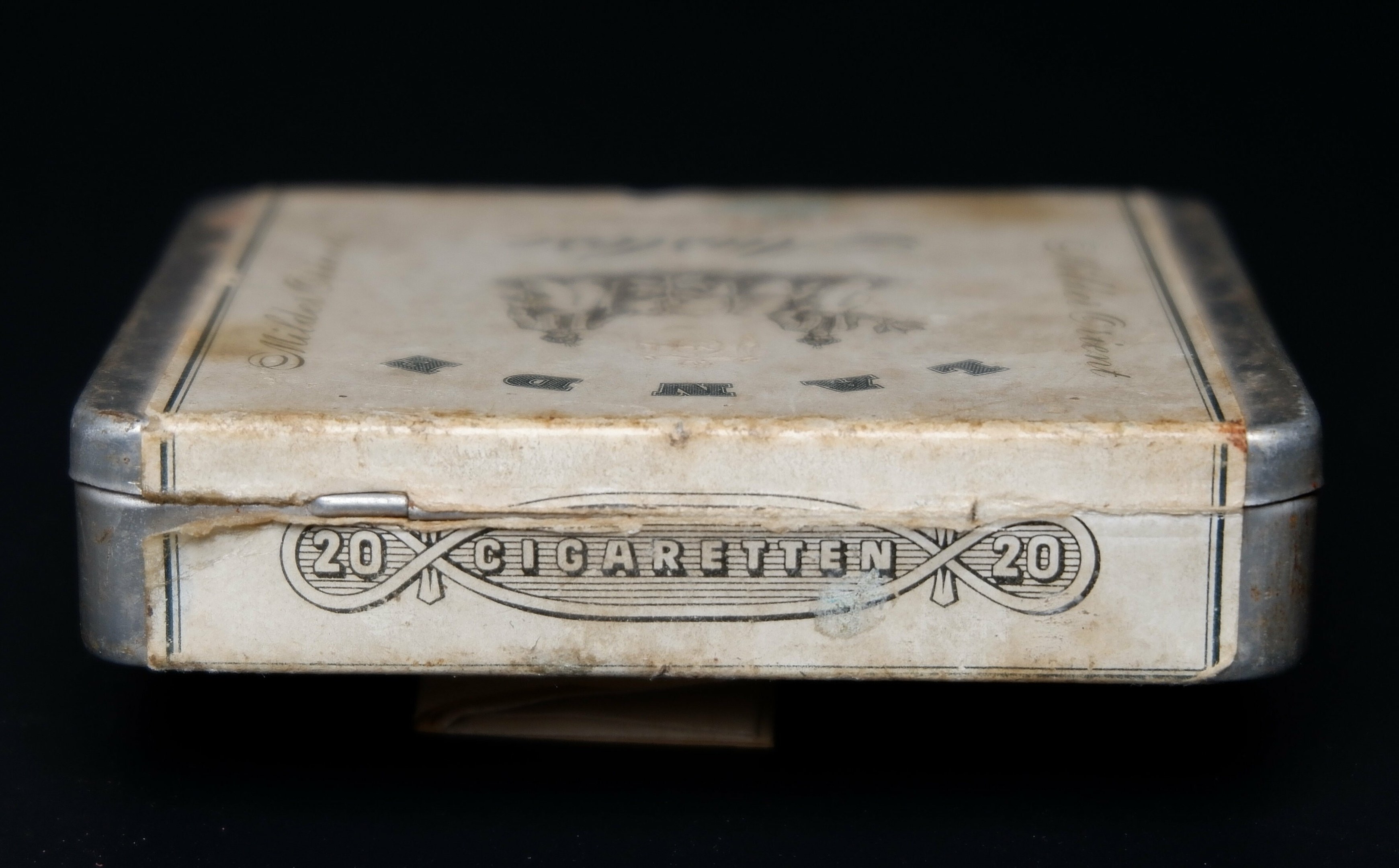 Alte Metall-Zigaretten-Dose mit Aufschrift auf einem schwarzen Tisch, die einen vintage-Eindruck vermittelt.