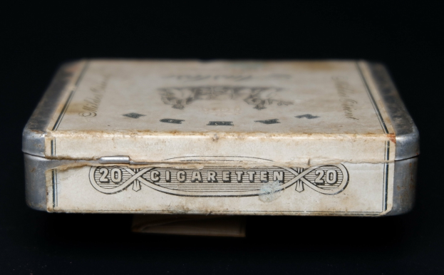 Alte Metall-Zigaretten-Dose mit Aufschrift auf einem schwarzen Tisch, die einen vintage-Eindruck vermittelt.