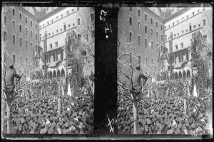 Ein Schwarz-Weiß-Foto einer großen Menschenmenge vor einem Gebäude mit Fenstern, Bäumen und Flaggen im Hintergrund, die scheinbar eine Demonstration abhalten, wobei einige Schilder und Transparente halten.