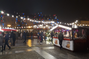 Ein nächtlicher Weihnachtsmarkt in der Stadt mit Menschen, beleuchteten Ständen, Gebäuden, Bäumen und festlicher Beleuchtung am Himmel.