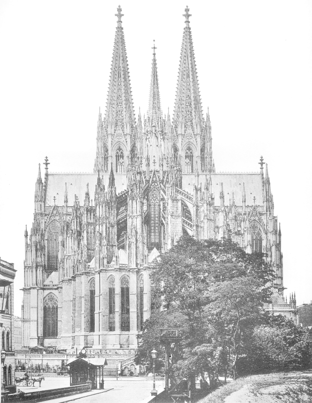 Ein Schwarz-Weiß-Foto des Kölner Doms in Köln, Deutschland, ein majestätisches Gebäude mit hohen Türmen und detaillierten Verzierungen, umgeben von Bäumen, Straßenlaternen, Menschen auf der Straße und dem Himmel im Hintergrund.