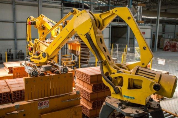 Großes Industriegebäude mit gestapelten Kisten, Überhead-Kränen, Zaun, Pfählen und einer fernen Wand in einer automatisierten Fertigungsumgebung.