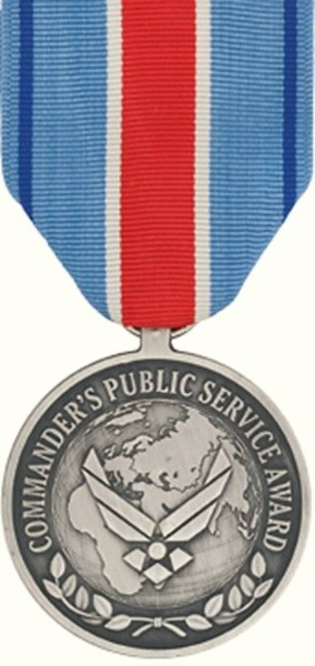 Eine Silbermedaille mit einem rot-weiß-blauen Band, auf dem der Text 'Commander's Public Service Award' auf einem weißen Hintergrund zu sehen ist.