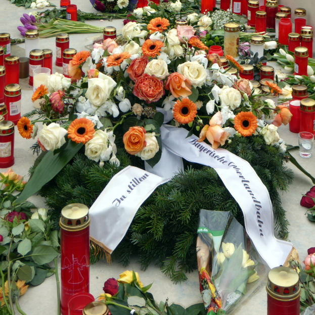 Mahnmal in Berlin, Deutschland, mit Blumen und Kerzen, die auf dem Boden vor einer Wand aufgestellt sind.