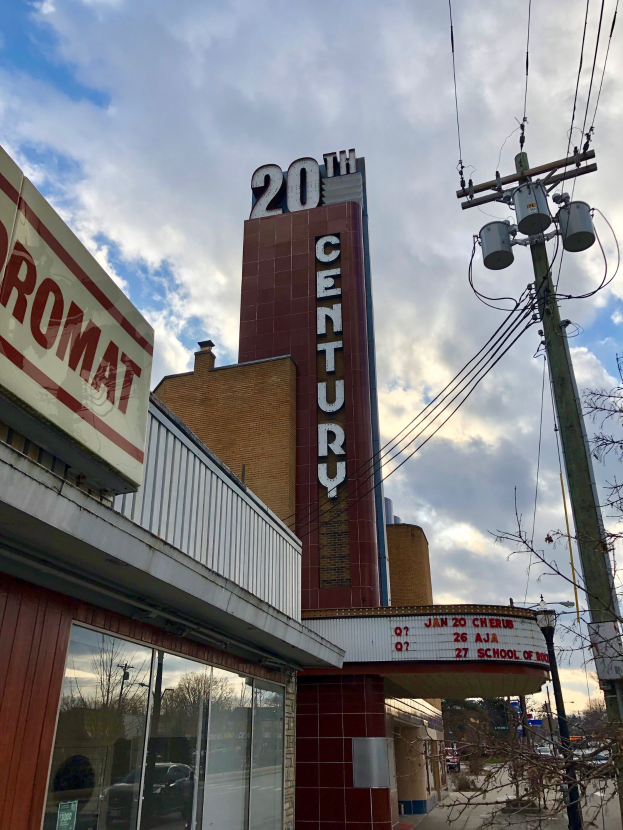 Außensicht des 20th Century Theatre in Detroit, Michigan, mit Glaswänden, Namensschildern, umgeben von Bäumen und Strommästen mit Drähten unter einem bewölktem Himmel.