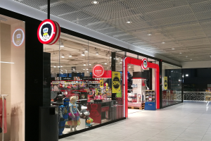 Ladenfront mit moderner, einladender Spielzeugauslage, Schaufensterpuppen und Texttafeln unter beleuchteten Decken und Glaswänden.