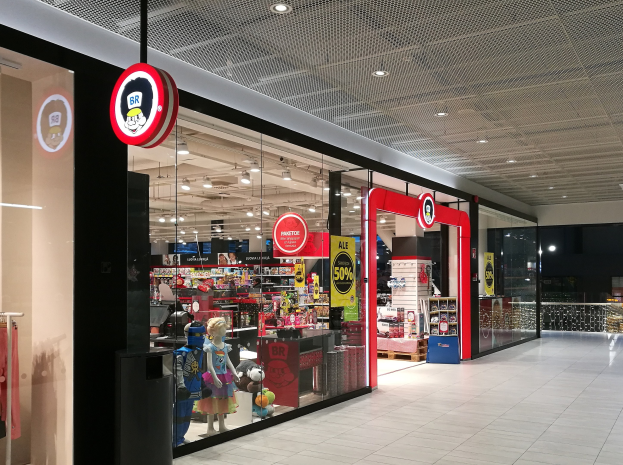 Ladenfront mit moderner, einladender Spielzeugauslage, Schaufensterpuppen und Texttafeln unter beleuchteten Decken und Glaswänden.