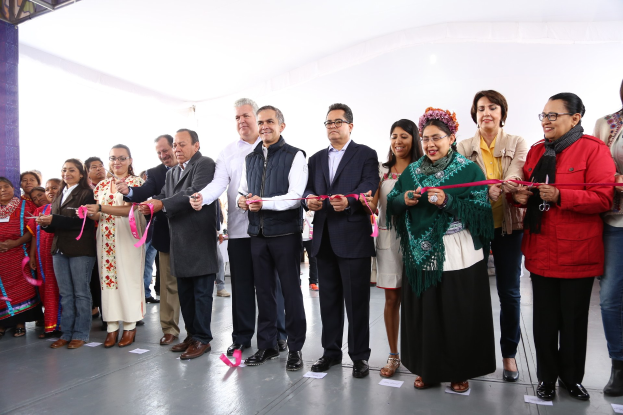 Eine Gruppe von Menschen bei einer Scherenschnitte-Zeremonie, die lächeln und Schere halten, mit Papieren auf dem Boden und einem weißen Tuch im Hintergrund.