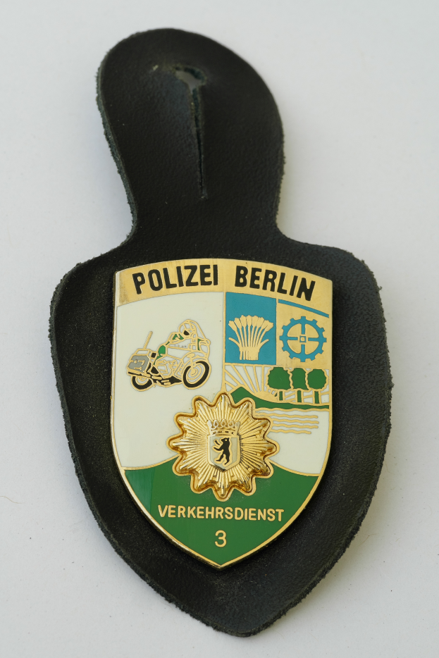 Ein Polizeistern mit der Aufschrift "Polizei Berlin" in fetter schwarzer Schrift auf einem blauen Schild mit einem weißen Stern und Rahmen.