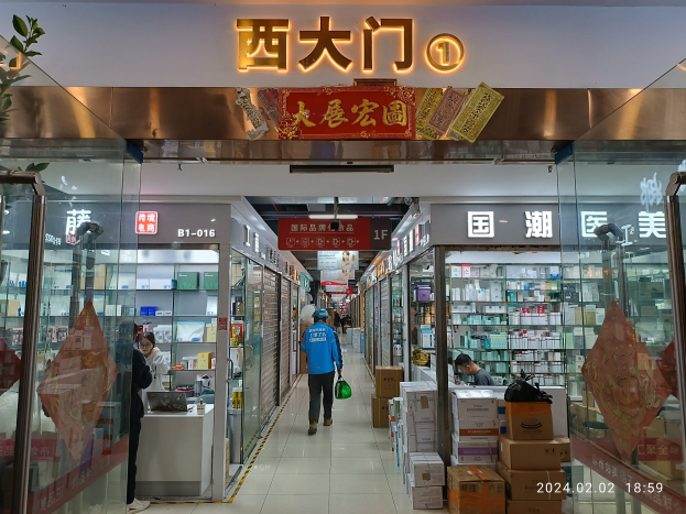 Innenansicht einer chinesischen Apotheke mit Glaswänden, Regalen voller Artikel, verstreuten Kartons, einer Pflanze links und einem Namensschild oben, das darauf hinweist, dass es sich um eine chinesische Drogerie handelt.