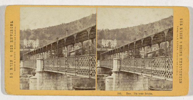 Schwarz-weiß-Foto einer Brücke über einen Fluss in Leipzig, Deutschland, mit Gebäuden, Bäumen und einem Hügel im Hintergrund.