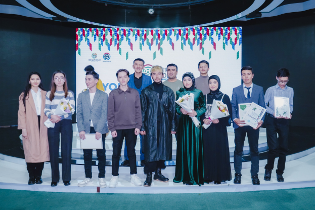 Gruppe von Menschen auf einer Bühne mit Blumensträuschen und Urkunden, mit einem "Jugend-Solar-Awards 2019"-Plakat im Hintergrund.