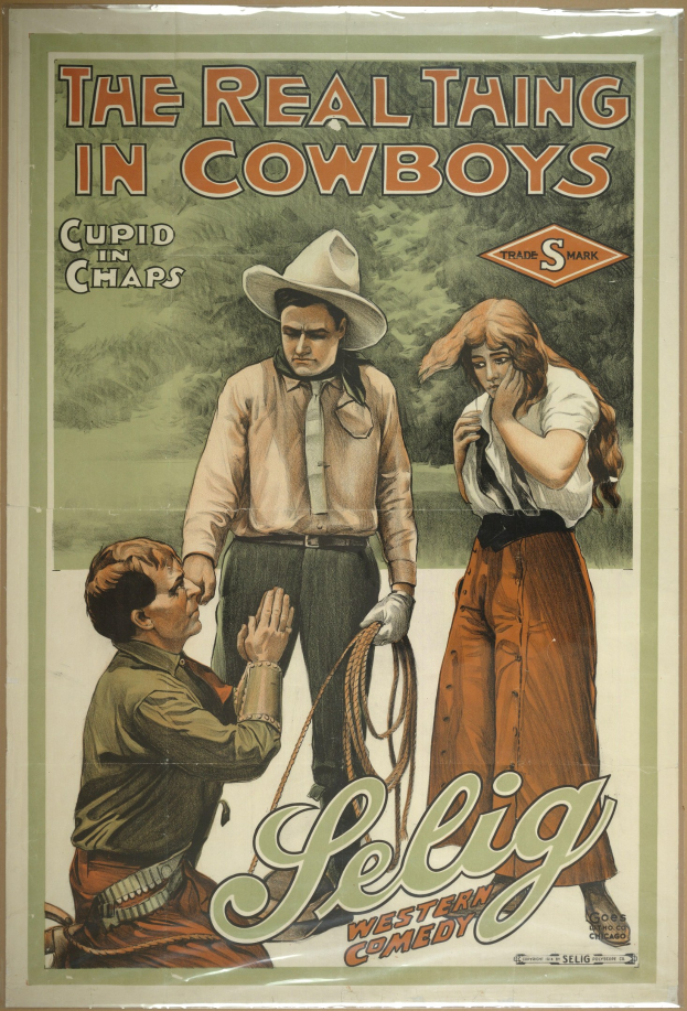 Plakat an einer Wand mit drei Personen (zwei Männer mit Cowboyhüten und eine Frau in einem langen Kleid) mit der Aufschrift "The Real Thing in Cowboys" in fetter schwarzer Schrift auf einem hellgelben Hintergrund.